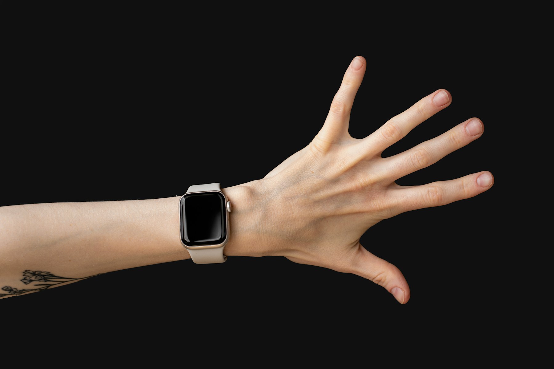A hand reaching out wearing an Apple Watch, display off, against a black background